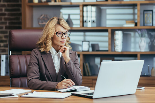 Elegant senior businesswoman concentrating while working at her home office with a laptop, pen, and notebook.