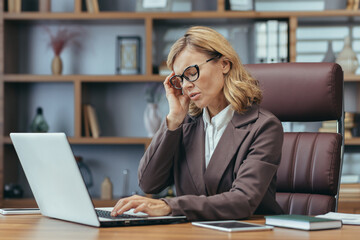 Fototapeta premium Elegant mature businesswoman concentrating as she works on a laptop from a well-appointed home office with tasteful decor.