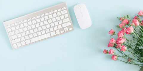 Female home office workplace with  keyboard, notepad, rose flowers, notebook on pastel blue background. Business minimal concept for women. Flat lay, top view, copy space, banner