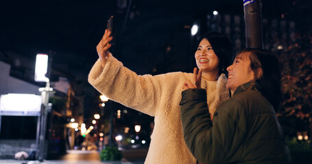 Japanese, women and selfie outdoor at night with hand gesture, peace sign and happy in city street....