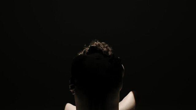 Portrait of male model silhouette on the black background in spotlight. Handsome man in underwear posing with his back at the camera.