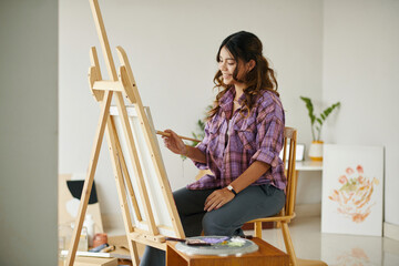 Smiling girl enjoying painting picture on easel in art class