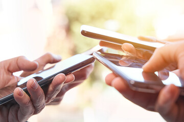 Four people's hands using smartphone on sunny summer afternoon. Connection and comunication