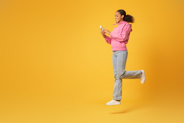 Happy African student jumps in mid air browsing smartphone, studio