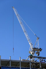 Fototapeta na wymiar Hoisting tower crane on the top section being constructed of modern high skyscraper building against blue cloudless sky