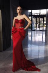beautiful woman with dark hair in elegant red dress with accessories posing in luxurious hotel lobby