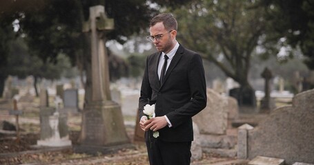 Funeral, cemetery and man with flower by tombstone for remembrance, burial ceremony and memorial service. Depression, sad and person with rose by gravestone for mourning, grief and loss in graveyard