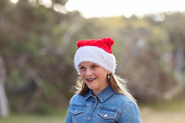 one girl with braces on her teeth wearing christmas hat outdoors with burry background