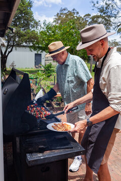 happy men cooking lunch food on bbq in backyard of country home