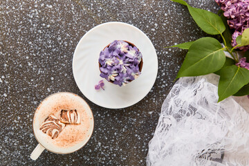 Aesthetic coffee break with trendy purple cake, coffee cup with melted marshmallow and lilac flowers.
