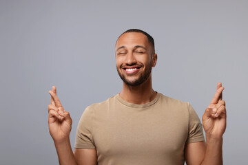 Happy man crossing his fingers on grey background