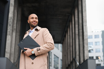 Happy man with clipboard outdoors, space for text. Lawyer, businessman, accountant or manager