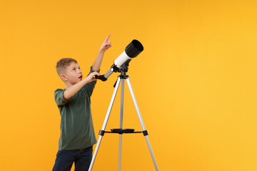 Surprised little boy with telescope pointing at something on orange background, space for text