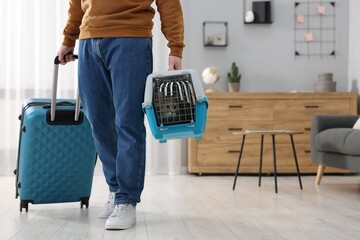 Travel with pet. Man holding carrier with cute cat and suitcase at home, closeup. Space for text - obrazy, fototapety, plakaty