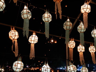beleuchtete, bunte Papier-Laternen bei Nacht mit Sky Lanterns im Hintergrund - Thailand Loy Krathong