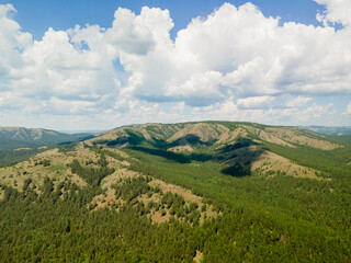 Fototapeta premium A beautiful sunrise landscape. Aerial view beautiful mountains covered with green pine forest against a background of blue sky with white clouds. Nature background. Photo from the drone.
