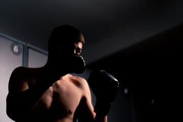Fototapeta na wymiar silhouette of a boy boxer in boxing gloves practicing his punches in the gym before training