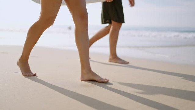 People with surfboards go on wet sand, low angle view. Surfers couple barefoot feet walk on wet sandy beach by sea surf. Footprints of man, woman going surfing on ocean waves on tropical island.