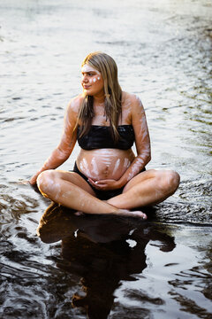 Expectant First nations Australian woman sitting in water on country in NSW Australia