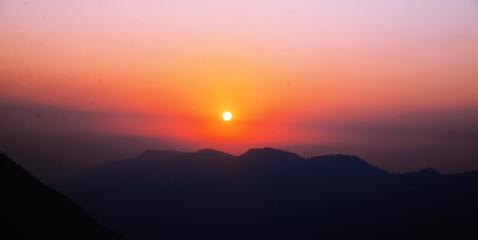 Obraz premium Sunset view in cinematic colors with mountains and sun setting behind, landscape wallpaper. Winter sunset view backdrop
