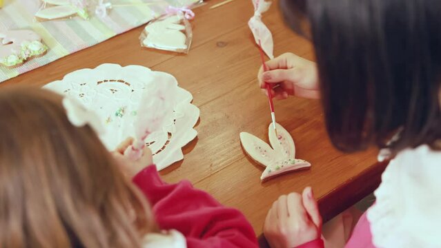 Focus on Feale hands decorating gingerbread in form on bunny ears. Easter holiday preparation of mother and daughter. Concept of holiday, Easter, family, motherhood and childhood