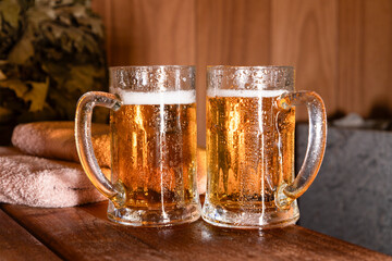 Couple of steamed mug of light fresh beer in the sauna on the shelf