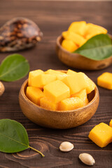 Dried mango cubes in wooden bowls on brown wooden, side view, selective focus.