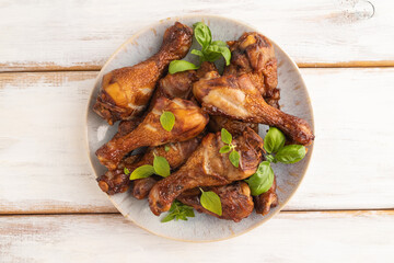 Smoked chicken legs on a ceramic plate on a white wooden background. Top view, close up.