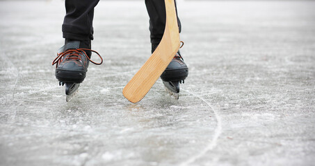 Ice skates and hockey stick close-up. Legs of a boy playing ice hockey on a frozen pond or in ice...