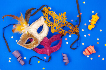 Three colorful masks together, isolated on a blue background adorned with confetti and streamers