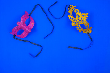 Two masks, one golden and the other violet, shiny and isolated on a blue background