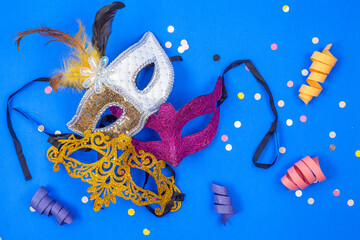 Three masks - gold, violet, and white, adorned with feathers - isolated against a blue backdrop