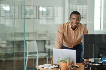 Smiling African businessman working with a laptop at his office desk - obrazy, fototapety, plakaty