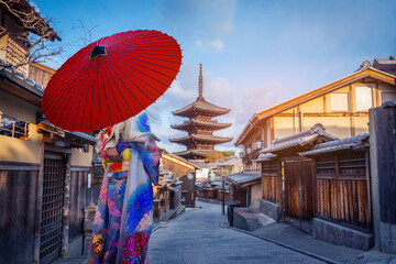 Asian woman wearing a Japanese kimono holding a red umbrella visits the Yasaka Pagoda.