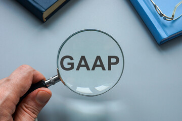 GAAP Generally Accepted Accounting Principles. A hand with a magnifying glass points to an...