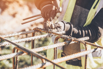 A worker uses steel tying wire to fasten steel rods to reinforcement bars close-up. Reinforced...
