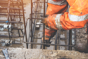 A worker uses steel tying wire to fasten steel rods to reinforcement bars close-up. Reinforced...