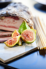 Guanciale affettato con fichi freschi e spaghetti crudi su un piatto quadrato, ingredienti
