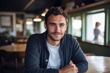 Thoughtful Young Eastern European Man with Stubble, Casually Dressed in Open-Collar Shirt, Gently Smiling in a Quaint Cafe during a Warm Afternoon