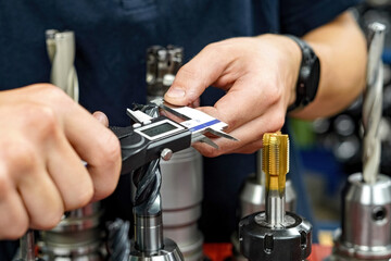 The worker operator of the cnc machine tool measures the cutting tool with a caliper for further...