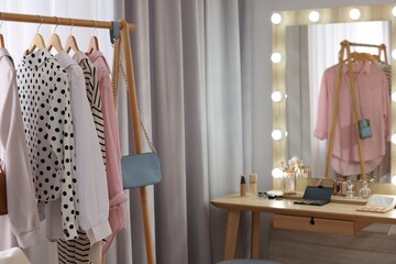Makeup room. Clothes rack and stylish mirror with light bulbs on dressing table indoors