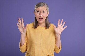 Portrait of surprised senior woman on violet background