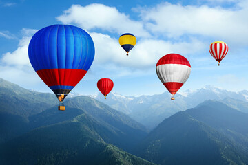 Bright hot air balloons flying in sky with clouds over mountains