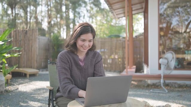 Young happy smiling Asain woman in cafe working video call facetime type project working on her laptop notebook personal computer, Female begins typing say hello on screen