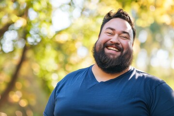 Man Laughing Joyfully Outdoors.
A joyful man in a blue shirt laughs heartily in a sunlit park, surrounded by greenery.