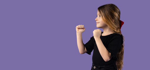 Horizontal picture of a little blonde girl dressed in black clothes in a fighting position, the concept of fighting training for children on a purple background.