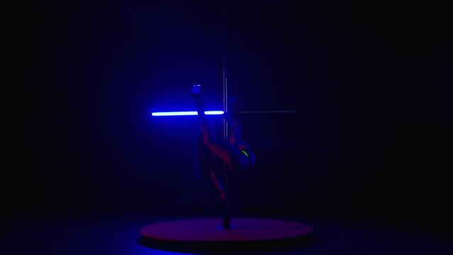 Woman doing erotic dance in dark studio coed by blue and red flashing light. Tight woman in yellow reflective lingerie practicing pole dance.