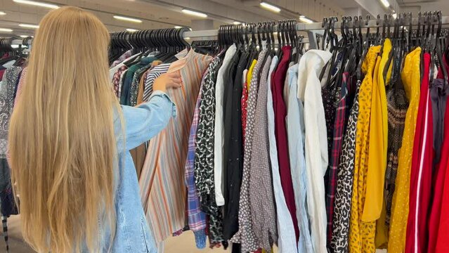 Selection of used clothes in a second-hand store. A woman buys inexpensive clothes