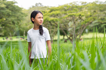 little brunette latina girl in the middle of a tall grass field looking towards the horizon
