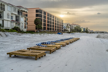​A row of double seating wooden chaise lounges, some with sun shade canopies dropped down, along...